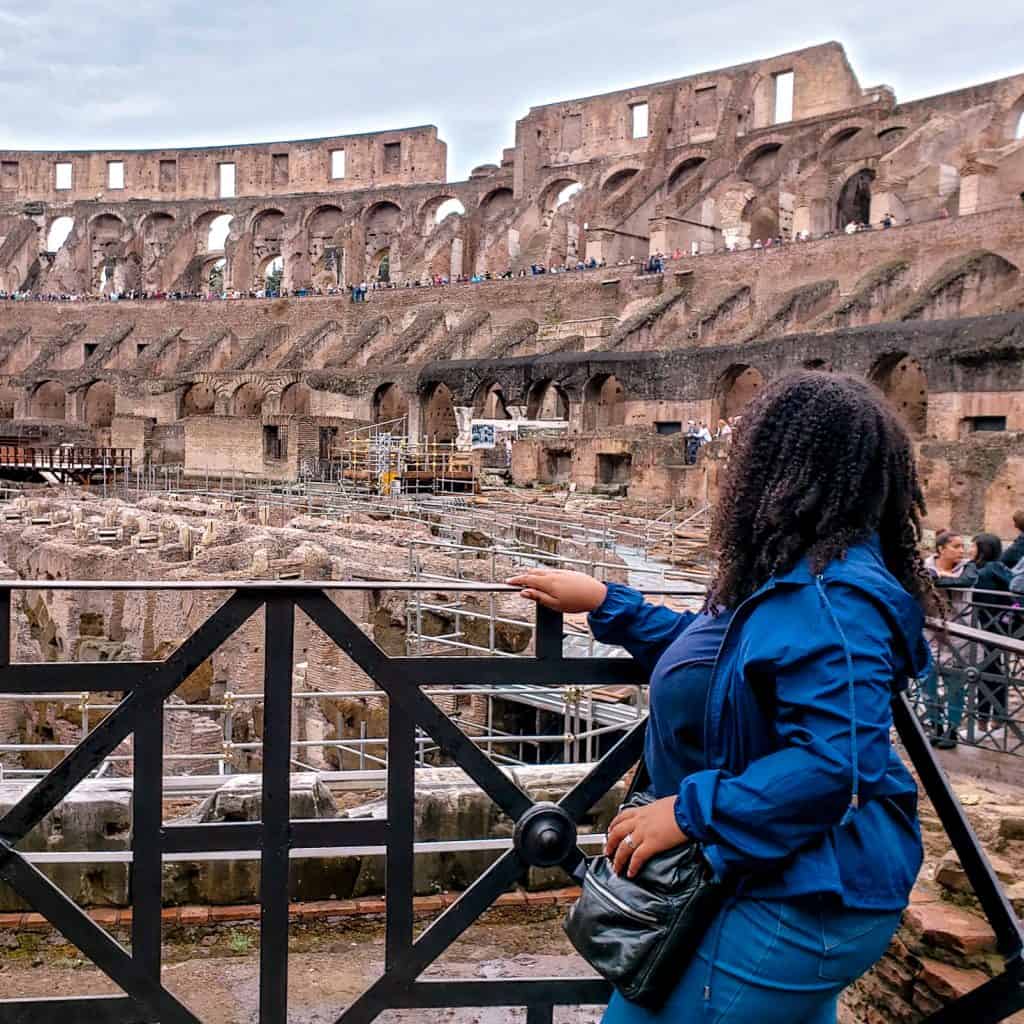 A woman is standing in front of the coliseum in rome.