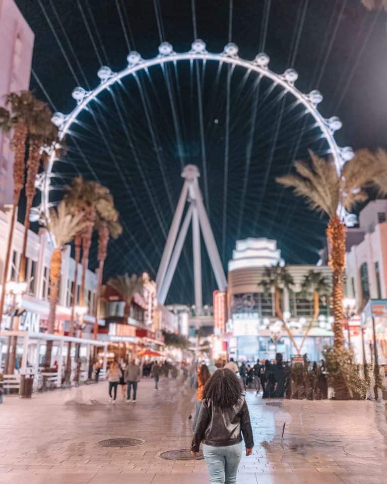 A woman walking in front of the ferris wheel in las vegas.