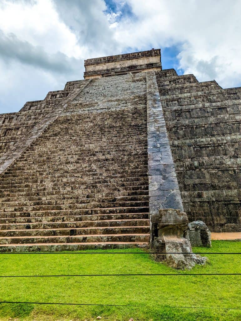 A stone pyramid with a stone head on top with chichen itza in the background.