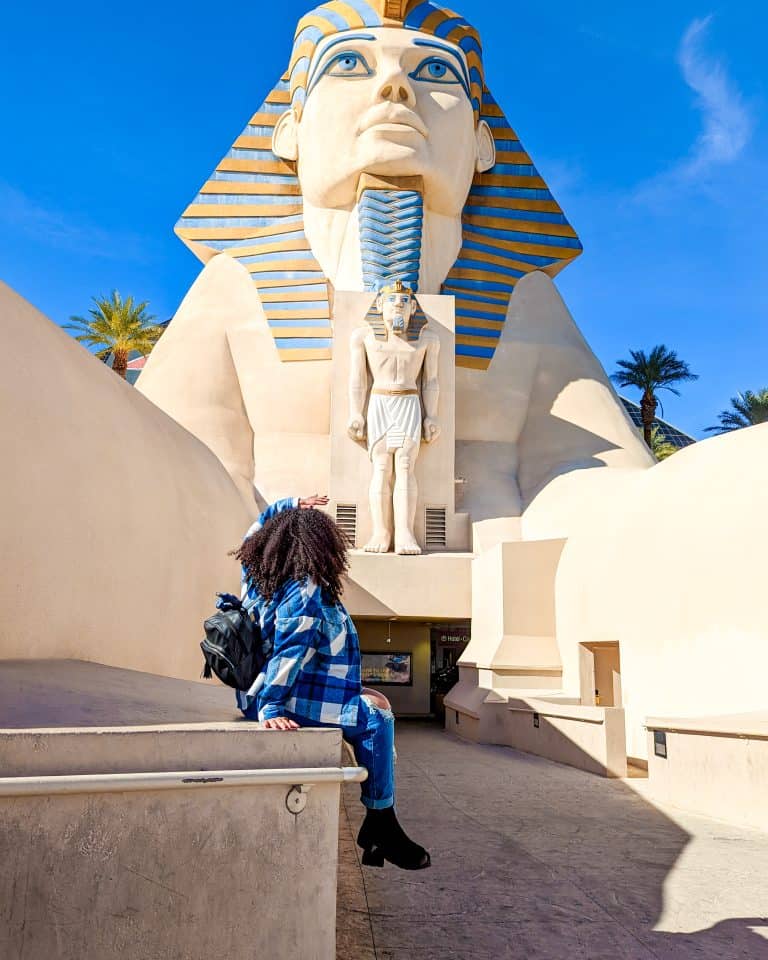 A woman sitting on a ledge in front of a statue of a man.