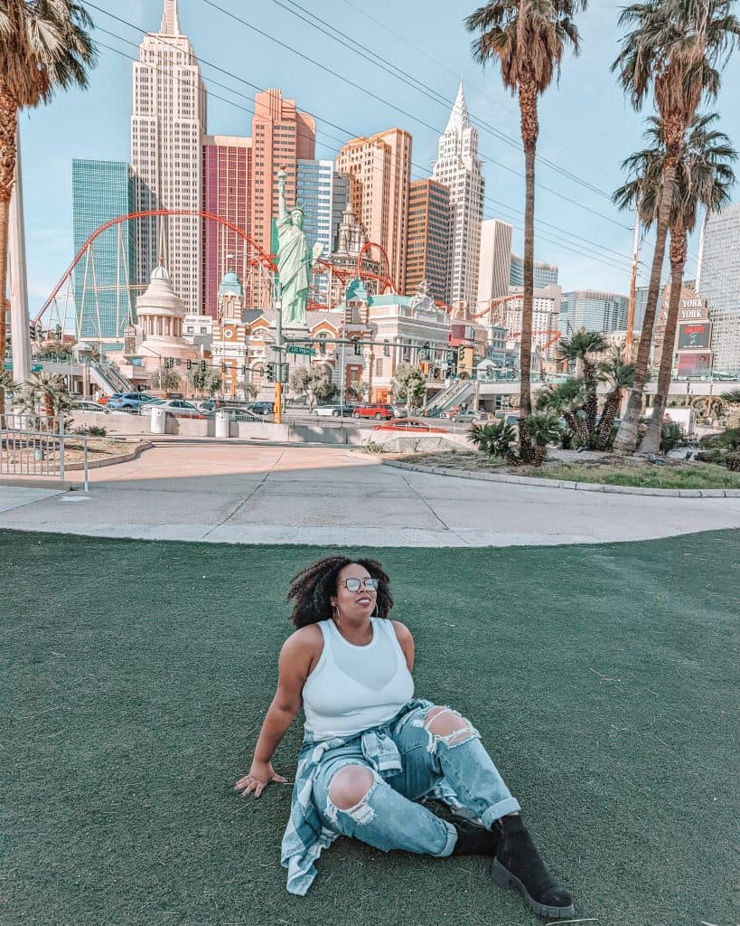 A woman sitting on grass in front of a city.