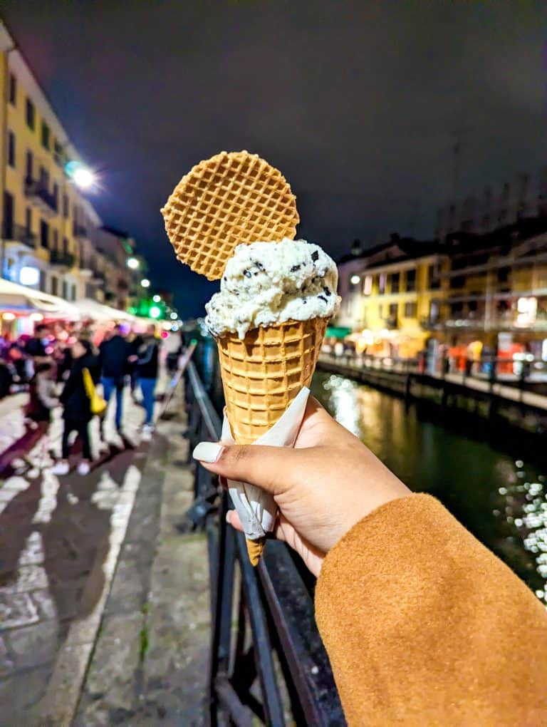 A person holding an ice cream cone in front of a canal.