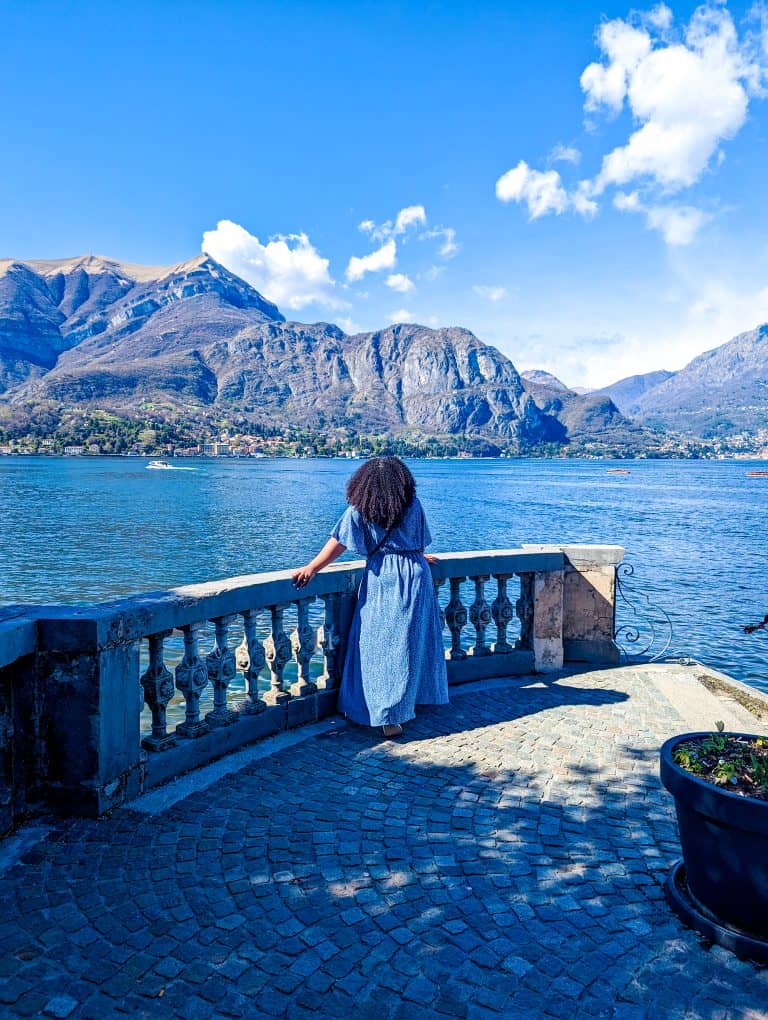 A woman in a blue dress is looking out over lake como.