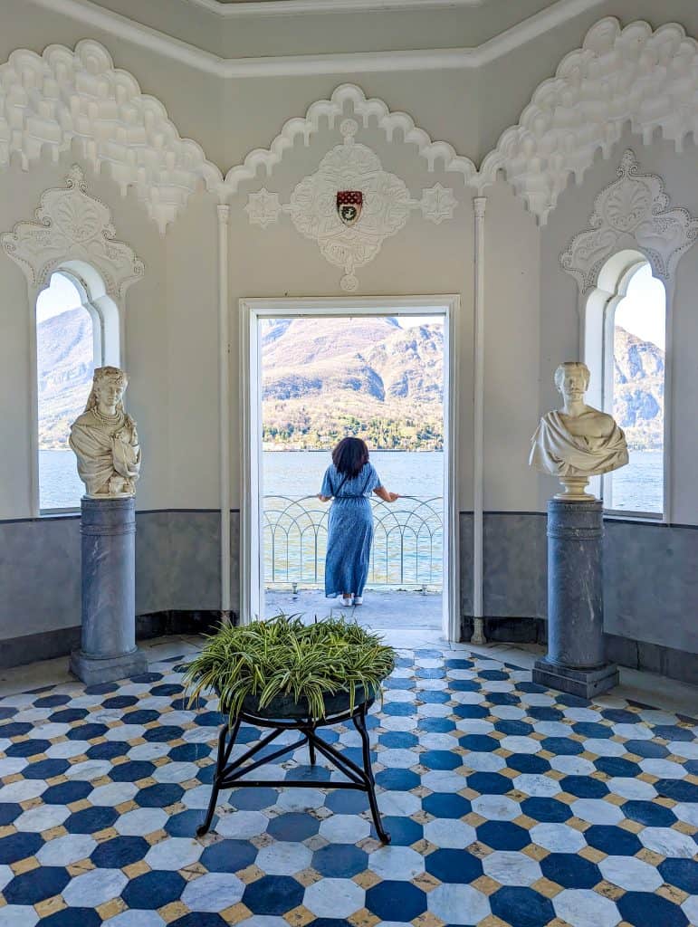 A woman is standing in a room with statues and a view of lake como.