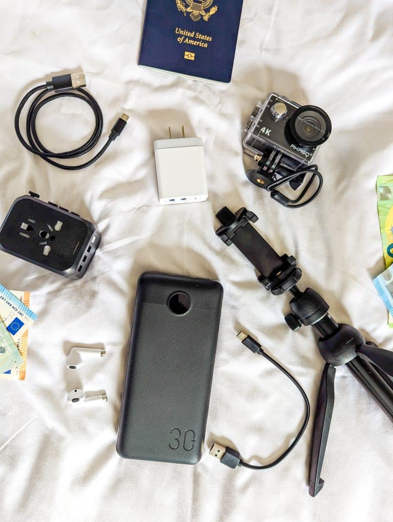 A bed with a cell phone, camera, passport and money.