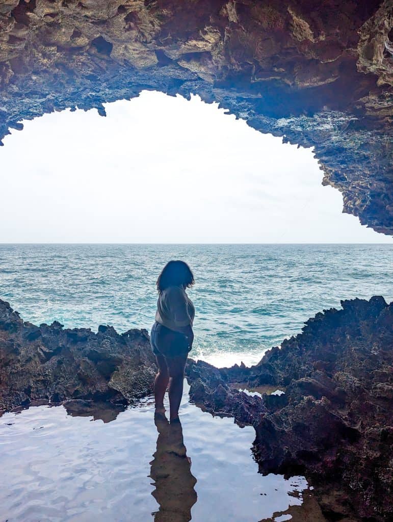 A woman standing in a cave looking at the ocean.