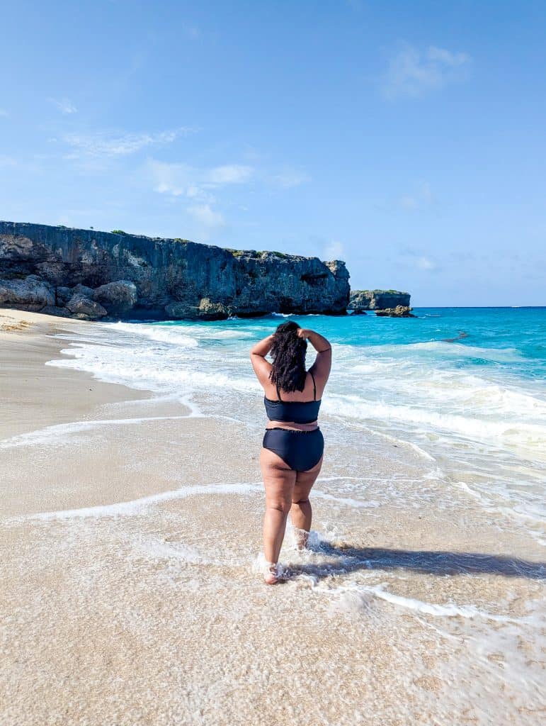 A woman in a black bikini walking on the beach.