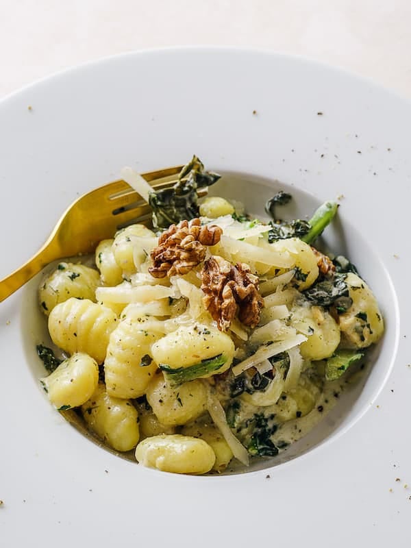 Gnocchi with walnuts and kale on a white plate.