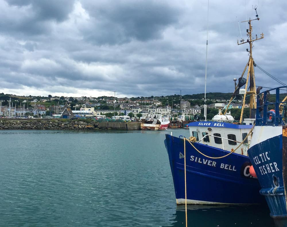 A serene blue boat docked in the water, with a seaside town in the back