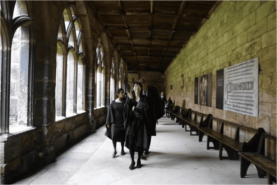 A group of people walking down a hallway in a school with robes on.