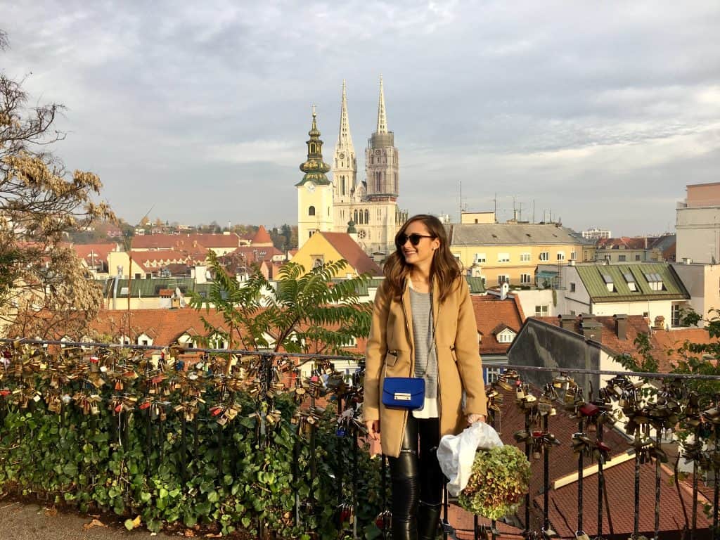 A woman standing on a balcony with a city in the background.
