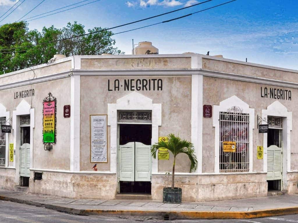 Corner view of "la negrita" cantina with closed green shutters and a clear blue sky, a popular spot for visitors looking for free things to do in Merida.