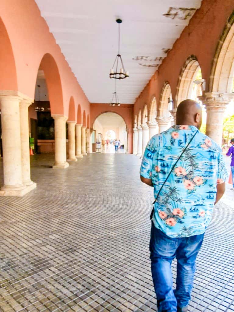 A man wearing a hawaiian shirt walking down a hallway.