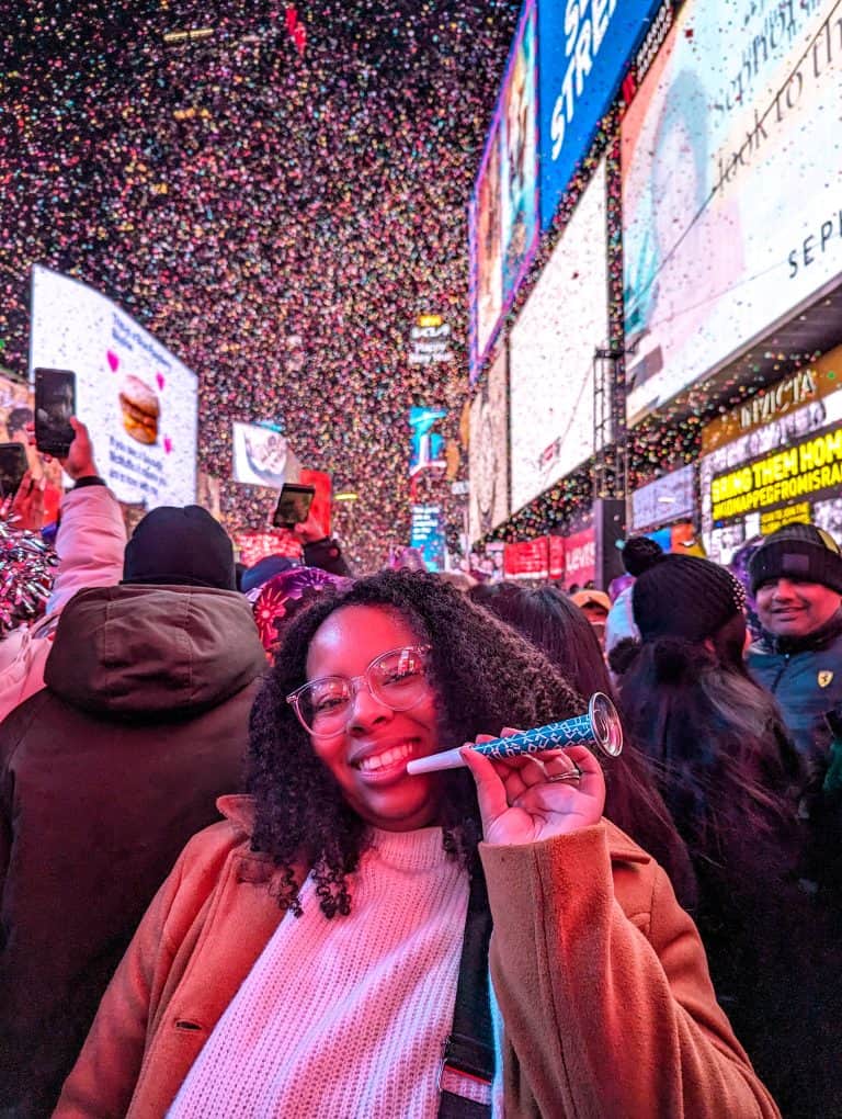 A woman is holding a blow horn in front of confetti in times square.