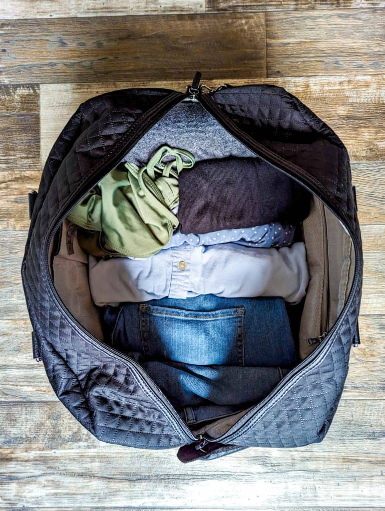 A duffel bag containing clothing sits on a wooden floor.