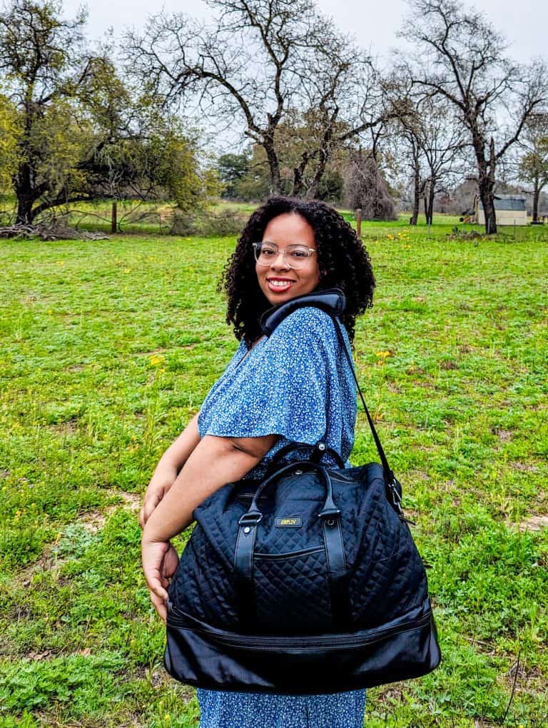 A woman carrying a black duffel bag in a field.