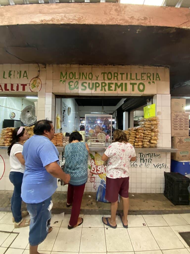 Customers purchasing goods at a traditional "molino y tortilleria" in a local market, experiencing one of the authentic things to do in Merida, Mexico.