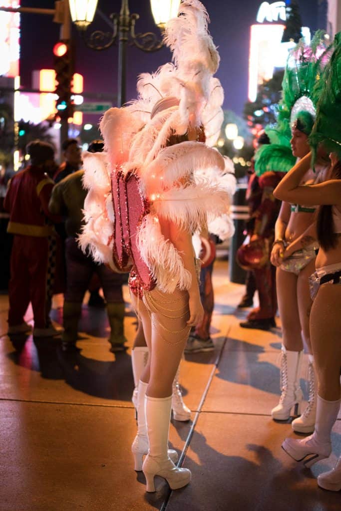 Performer in a feather costume and heeled boots on a Las Vegas street at night.