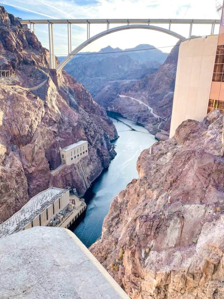 The hoover dam and the mike o'callaghan–pat tillman memorial bridge viewed from a high vantage point, showcasing the colorado river and surrounding rocky terrain.