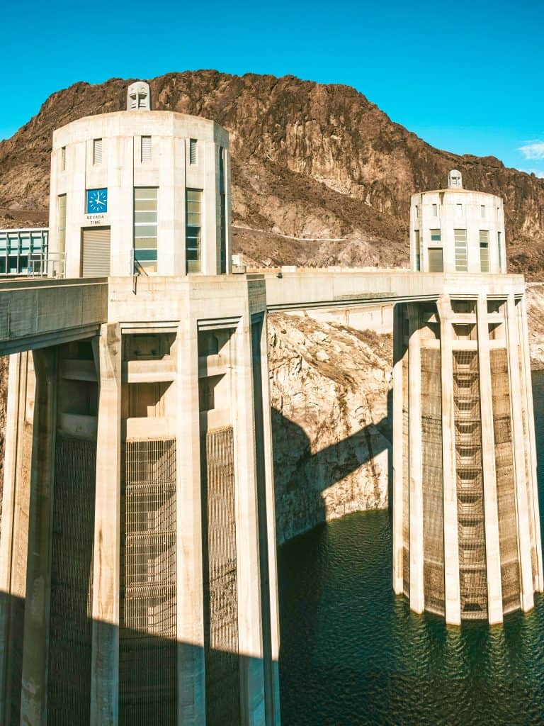 Massive concrete dam with intake towers against a rugged mountain backdrop.