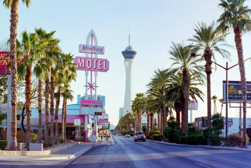 A street view featuring the monterey motel sign with the stratosphere tower in the background, lined by palm trees under a clear sky.