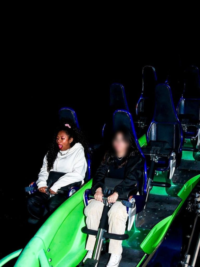 Two people on a dark roller coaster, one looking thrilled.
