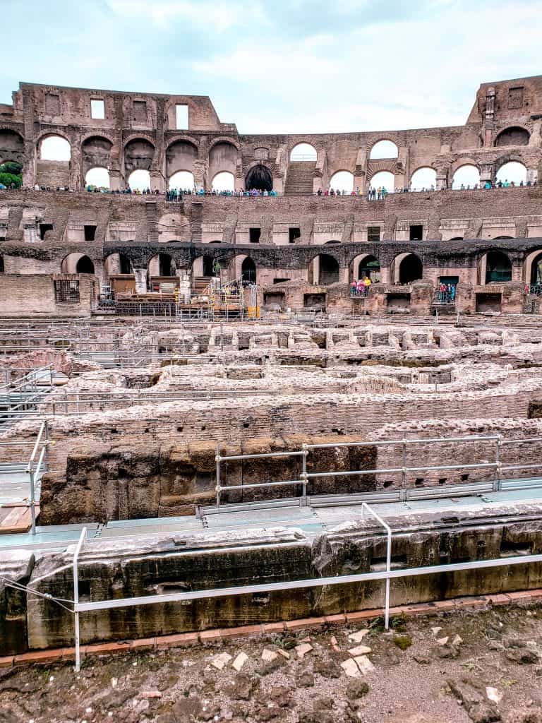 Best way to see the Colosseum: interior view with visible underground structures and tourists walking along the upper levels.