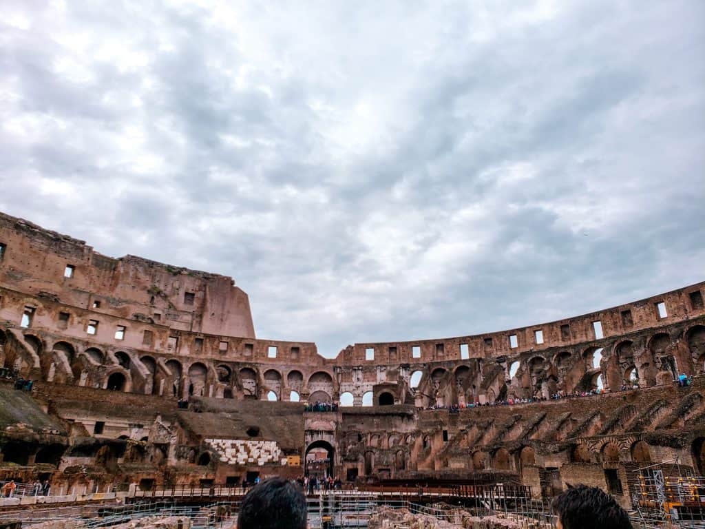 Interior view of the colosseum, showcasing the best way to see ruins and tourists under a cloudy sky.