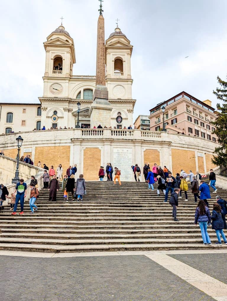 Tourists climbing the spanish steps in rome, with the trinità dei monti church in the background.