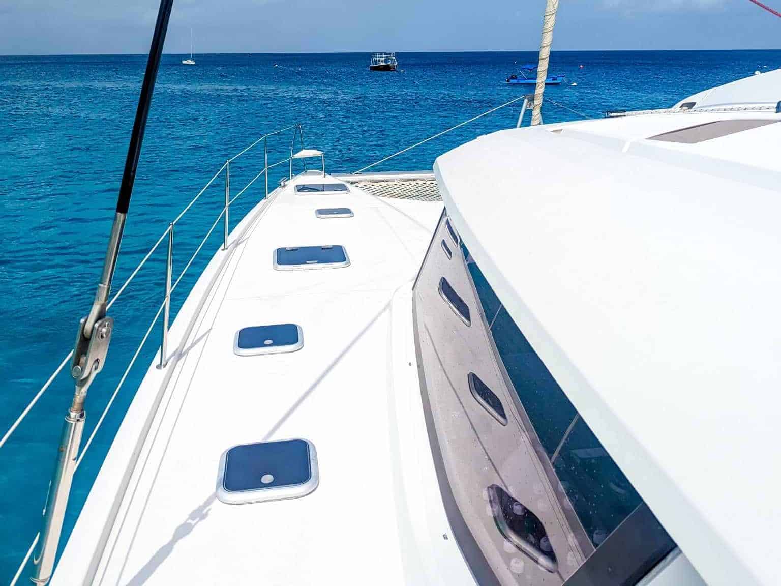 View from the deck of a boat cruising on clear blue water under a sunny sky with fluffy clouds.