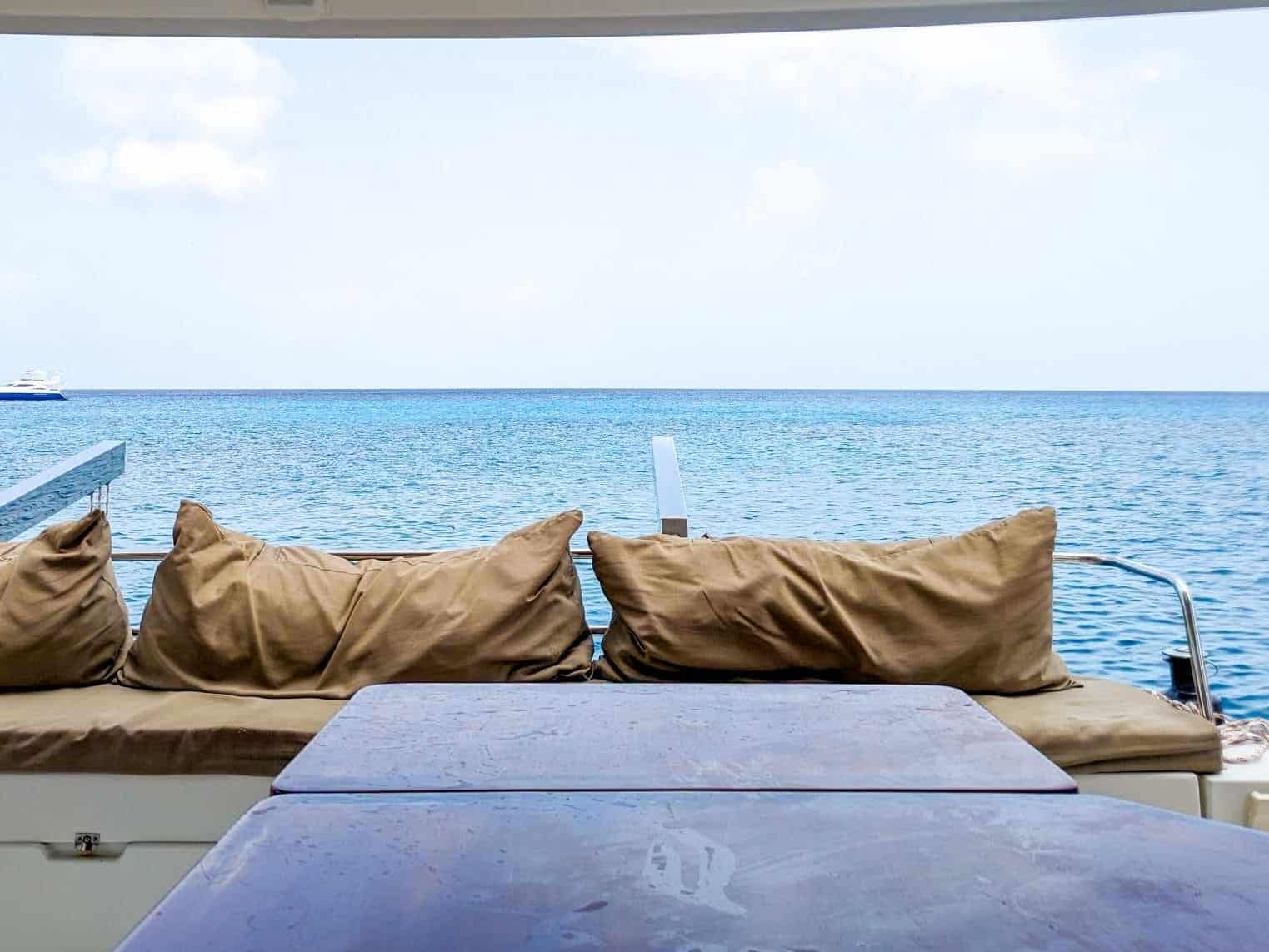 View of the ocean from a yacht's seating area, featuring cushioned benches and a wooden table.