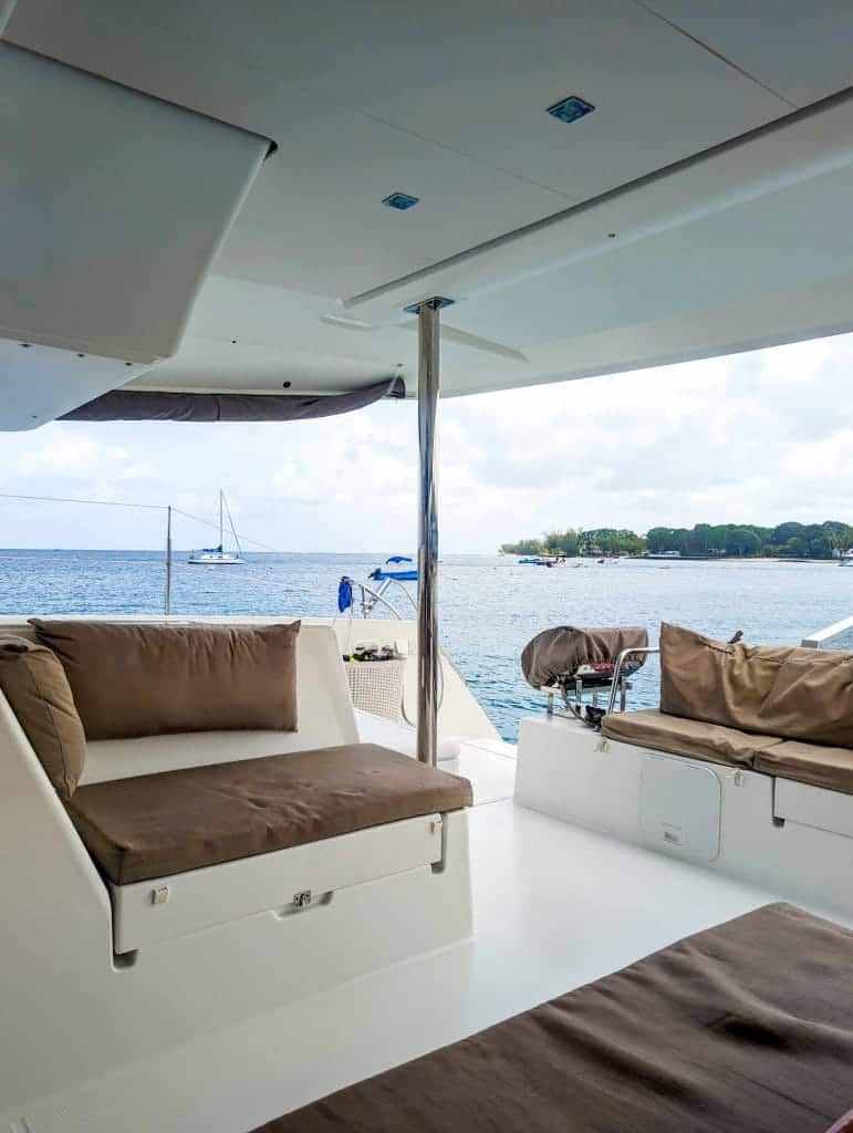A boat with cushioned seating overlooks calm ocean waters and a distant shoreline with a sailboat.