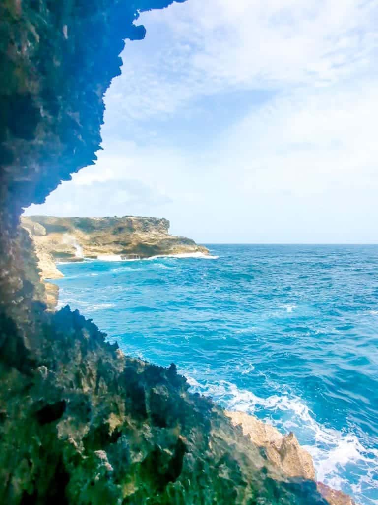 Rocky coastline with blue ocean waves and a partly cloudy sky. Cliffside is visible in the foreground.