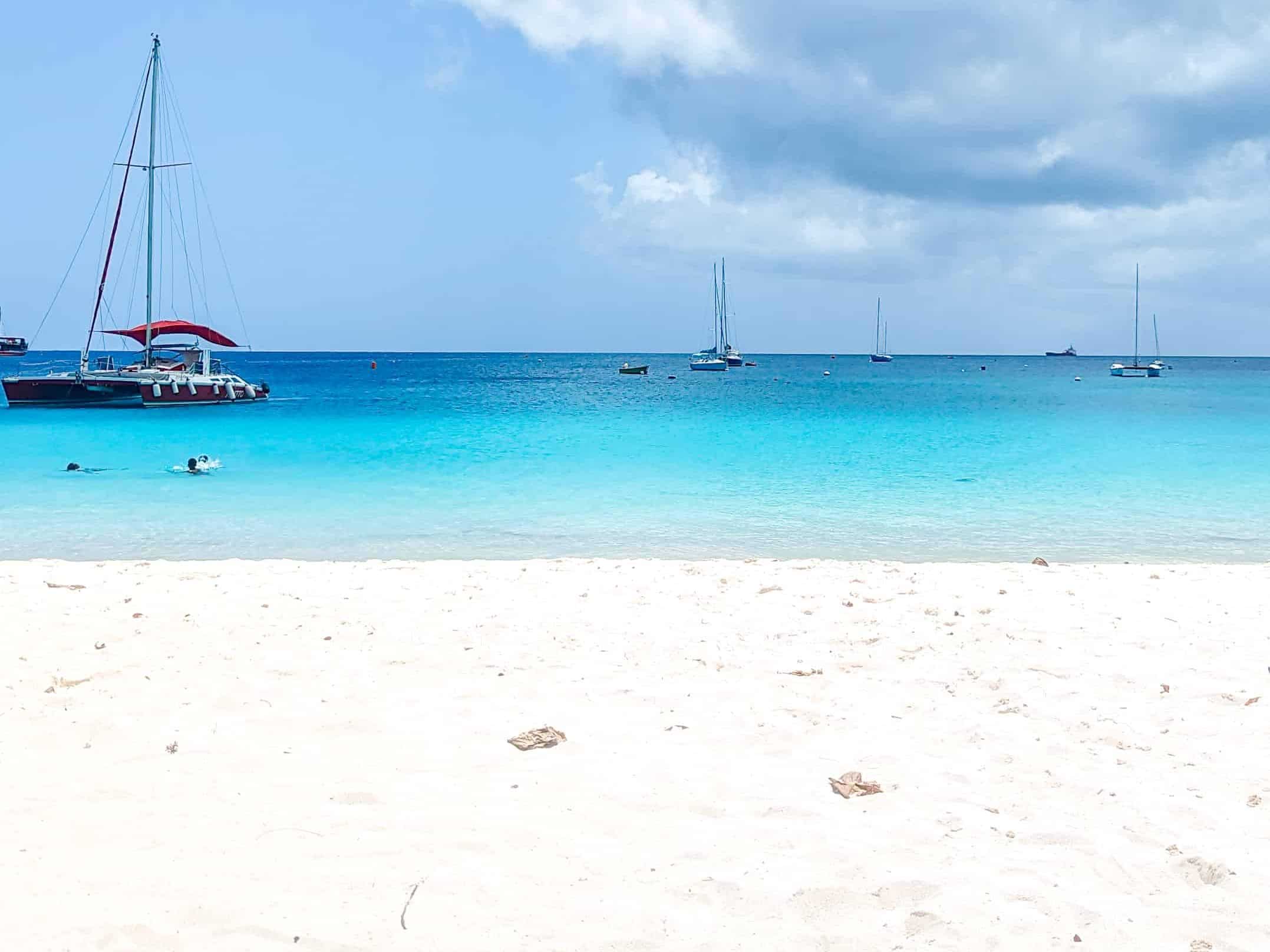 A person's feet under an umbrella on a beach.