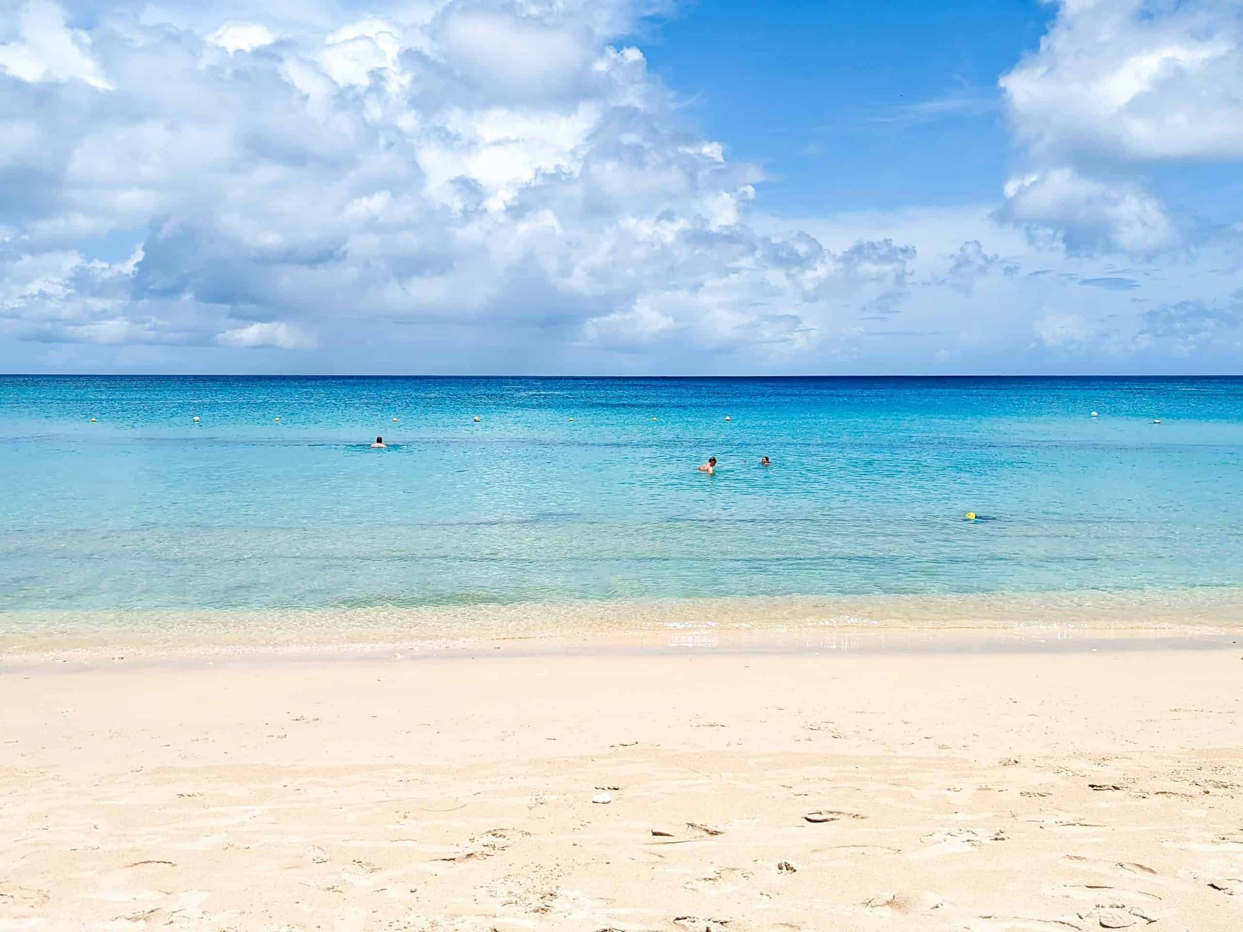 A sandy beach with blue water and white clouds.