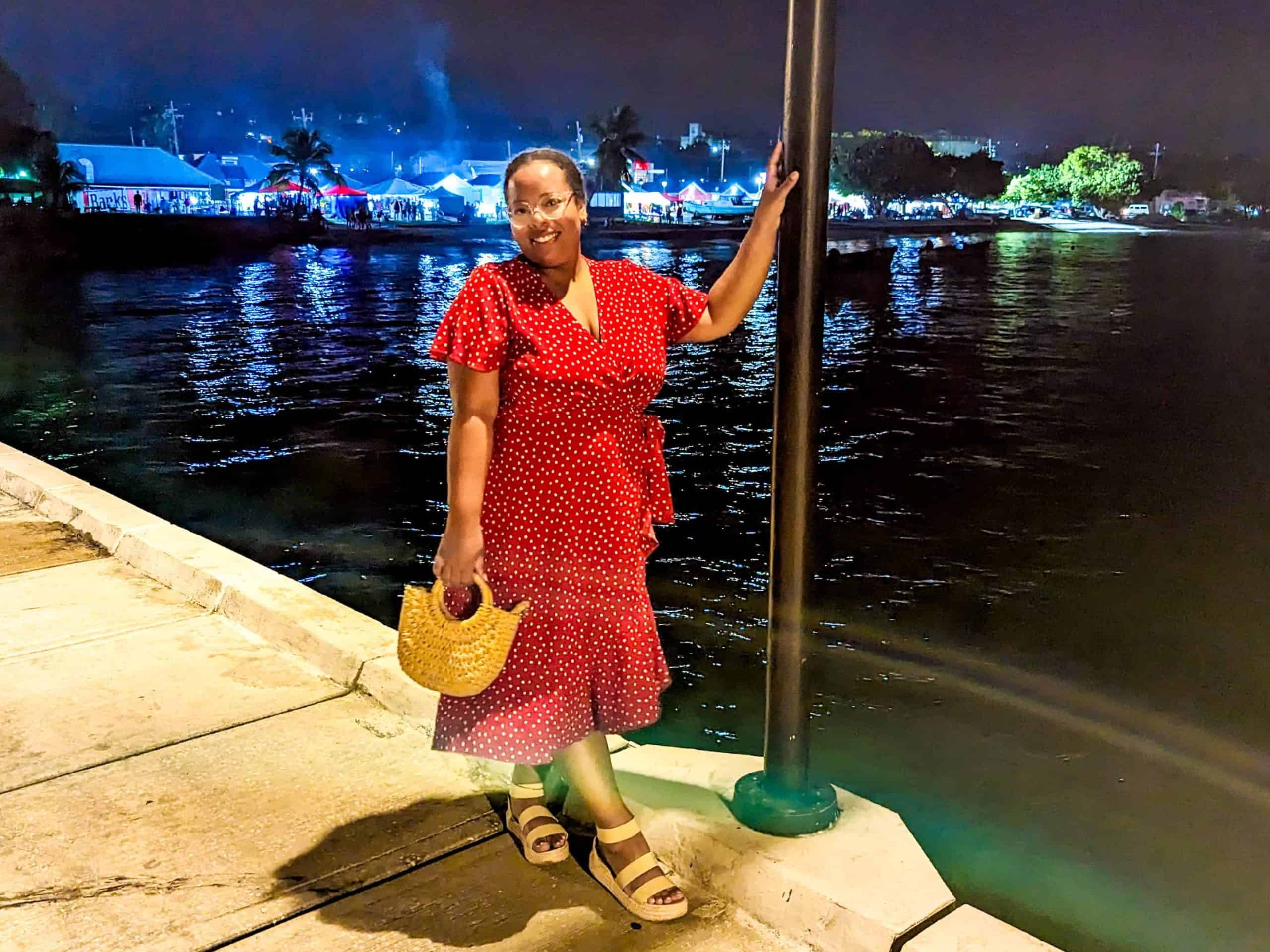 A woman in a red dress standing on a dock at night.